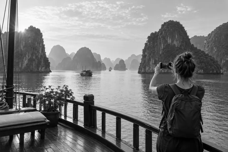 A traveller photographs the limestone islands of Ha Long Bay from a boat deck.